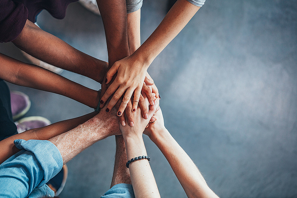 Friends with stack of hands showing unity and teamwork.